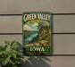 A vintage-style metal sign for Green Valley State Park in Iowa, featuring a scenic landscape with a river, cliffs, and pine trees.