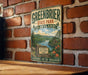 A vintage-style metal sign for Greenbrier State Park, Maryland, featuring a scenic landscape with mountains, lakes, and a cabin.
