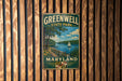 A vintage metal sign for Greenwell State Park in Maryland, featuring a scenic landscape with a lake, trees, and a sailboat.