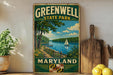 A vintage-style metal sign for Greenwell State Park in Maryland, featuring a scenic landscape with a lake, trees, and a sailboat.
