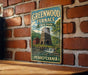 A vintage-style metal sign for Greenwood Furnace State Park in Pennsylvania, featuring a brick wall and a small waterfall in the background.