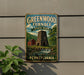 A vintage-style metal sign for Greenwood Furnace State Park in Pennsylvania, featuring a red brick building and a stone chimney with a waterfall in the background.