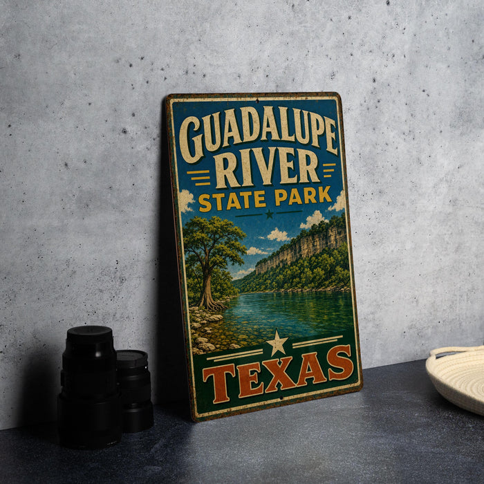 A vintage-style metal sign for Guadalupe River State Park in Texas, featuring a scenic landscape with a river, mountains, and trees.