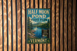 A vintage-style metal sign for Half Moon Pond State Park in Vermont, featuring a scenic landscape with a lake and mountains.