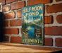 A vintage-style metal sign for Half Moon Pond State Park in Vermont, featuring a scenic illustration of the pond surrounded by mountains and pine trees.