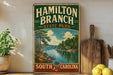 A vintage-style sign for Hamilton Branch State Park in South Carolina, featuring a scenic landscape with a river and pine trees.