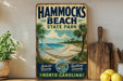 A vintage-style sign for Hammocks Beach State Park in North Carolina, featuring a beach scene with palm trees and a hammock.