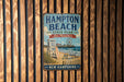 A vintage metal sign for Hampton Beach State Park in New Hampshire, featuring a beach scene with a lifeguard tower and a ferris wheel.