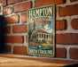 A vintage metal sign for the historic site of Hampton Plantation in South Carolina, featuring a building and palm trees.