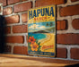 A vintage metal sign for Hapuna Beach, Hawaii, featuring a beach scene with palm trees and a blue sky.