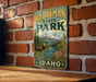 A vintage metal sign for Harriman State Park in Idaho, featuring a moose and a mountain landscape.