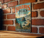 A vintage metal sign for Harris Beach State Park in Oregon, featuring a scenic landscape with mountains, water, and pine trees.