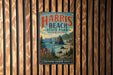 A vintage metal sign for Harris Beach State Park in Oregon, featuring a scenic coastal landscape with mountains, pine trees, and a body of water.