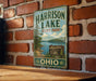 A vintage metal sign for Harrison Lake State Park in Ohio, featuring a scenic landscape with a lake and trees.