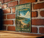 A vintage metal sign for Harrisville State Park in Michigan, featuring a scenic landscape with a lake, beach, and mountains.
