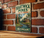 A vintage metal sign for Hartwick Pines State Park in Michigan, featuring a scenic illustration of a cabin and a river surrounded by pine trees.