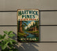 A vintage metal sign for Hartwick Pines State Park in Michigan, featuring a scenic illustration of a cabin and pine trees along a river.
