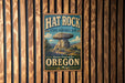 A vintage-style metal sign for the Hat Rock State Heritage Site in Oregon, featuring a large rock formation and the text "Discover Oregon's Past" and "Oregon".