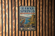 A metal sign with the text "HAWKS SPRINGS STATE RECREATION AREA Wyoming" is displayed on a wooden wall.