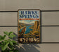 A vintage-style sign for the state recreation area of Hawks Springs, Wyoming, featuring a scenic landscape with a bird of prey and a river.