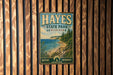 A vintage metal sign for Hayes State Park, Michigan, featuring a scenic landscape with a beach, mountains, and pine trees.