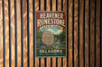 A vintage-style metal sign for Heavener Runestone State Park in Oklahoma, featuring a scenic illustration of a river and a large rock.