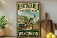 A vintage-style metal sign for Heritage Hill State Historical Park in Wisconsin, featuring an illustration of a historic building, church, and horse-drawn carriage.