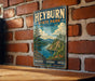 A vintage-style metal sign for Heyburn State Park in Idaho, featuring a scenic landscape with a lake and mountains.