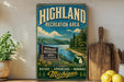 A vintage-style metal sign for the Highland Recreation Area in Michigan, featuring a scenic landscape with a lake, mountains, and pine trees.