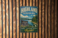 A vintage metal sign for the Highland Recreation Area in Michigan, featuring a scenic landscape with a river, mountains, and pine trees.