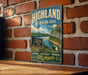 A vintage metal sign for the Highland Recreation Area in Michigan, featuring a scenic landscape with a lake and mountains.