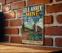 A vintage-style metal sign for Hill Annex Mine in Minnesota, featuring a scenic image of the mine and surrounding landscape.