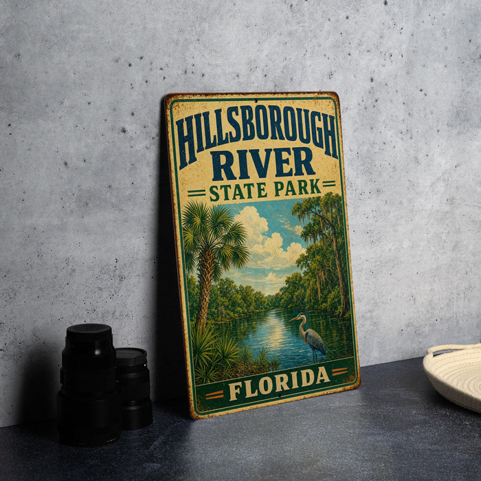 A vintage-style sign for Hillsborough River State Park in Florida, featuring a scenic illustration of the river surrounded by palm trees and a heron.