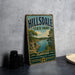 A vintage-style sign for Hilldale State Park in Kansas, featuring a scenic landscape with a lake and mountains.