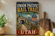 A vintage-style metal sign for the Union Pacific Rail Trail in Utah, featuring a scenic image of a bridge and mountains.