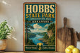 A vintage-style sign for Hobbs State Park in Arkansas, featuring a scenic landscape with a river, mountains, and pine trees.