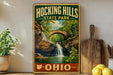 A vintage-style sign for Hocking Hills State Park in Ohio, featuring a scenic image of a waterfall surrounded by lush greenery.