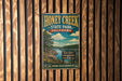 A vintage-style metal sign for Honey Creek State Park in Oklahoma, featuring a scenic landscape with a river, trees, and a cloudy sky.