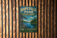 A vintage-style metal sign for Hopeville Pond State Park in Connecticut, featuring a scenic landscape with pine trees, a lake, and mountains.