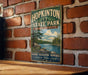 A vintage metal sign for Hopkinton State Park in Massachusetts, featuring a scenic landscape with a lake and pine trees.