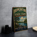 A vintage metal sign for Hopkinton State Park in Massachusetts, featuring a scenic landscape with pine trees, a lake, and mountains.