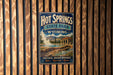 A vintage-style metal sign for Hot Springs State Park in Wyoming, featuring a scenic image of the park's natural hot springs.