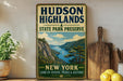 A vintage-style sign for Hudson Highlands State Park Preserve, featuring a scenic mountain landscape with a river and a boat, is displayed on a shelf next to a wooden cutting board and some lemons.