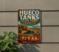 A vintage-style metal sign for Hueco Tanks State Park & Historic Site in Texas, featuring a desert landscape with a small lake and mountains in the background.