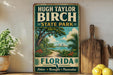 A vintage-style sign for Hugh Taylor Birch State Park in Florida, featuring a tropical landscape with palm trees, a beach, and a city skyline in the background.