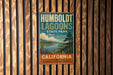 A vintage metal sign for Humboldt Lagoon State Park in California, featuring a scenic landscape with a lake, mountains, and a tree.