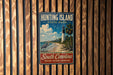 A vintage-style metal sign for Hunting Island State Park, featuring a lighthouse, beach, and birds, is displayed on a wooden fence.
