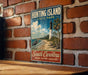 A vintage-style metal sign for Hunting Island State Park, featuring a lighthouse and a beach scene, is displayed on a brick wall.