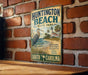 A vintage metal sign for Huntington Beach State Park, featuring a seagull and a lighthouse, is displayed on a brick wall.