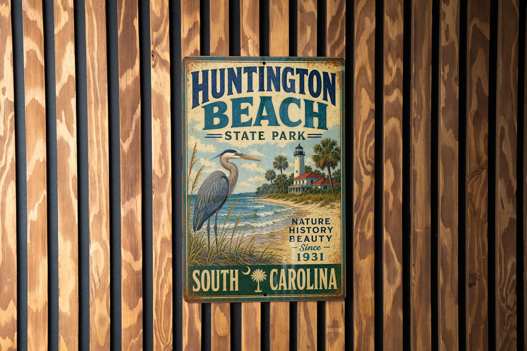 A vintage metal sign for Huntington Beach State Park in South Carolina, featuring a heron and a lighthouse, is displayed on a wooden wall.
